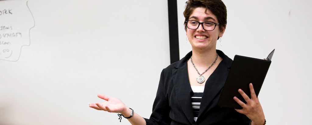 A student presents her research, notebook in hand.